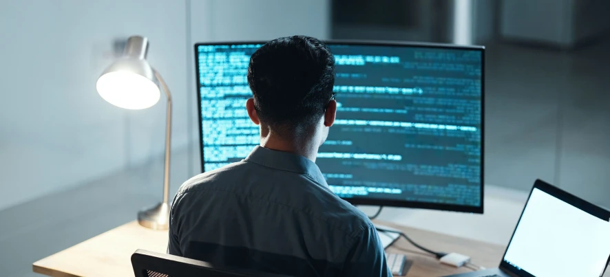 Developer working at a desk with code on multiple screens