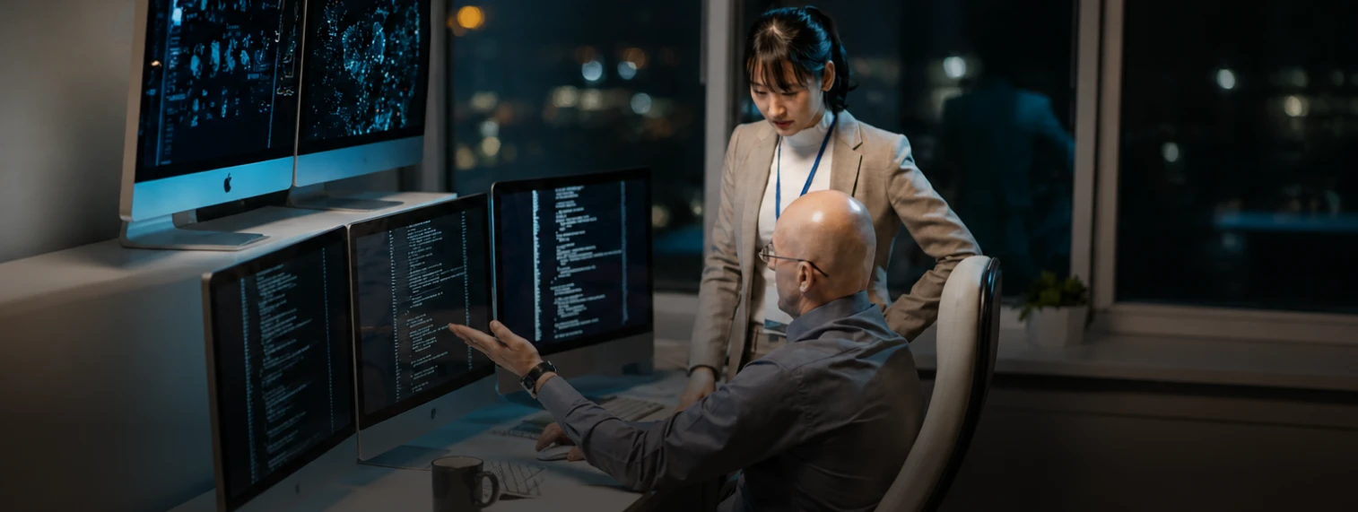 Engineers reviewing code on multiple monitors at night